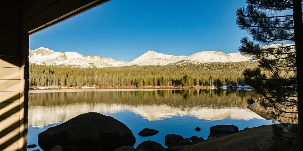 Snowy mountain peaks and forest reflected on crystal-clear lake under bright blue sky.