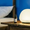 Flacon d’huile de CBD posé sur une table de nuit en bois à côté d’une lampe allumée.