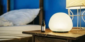 Flacon d’huile de CBD posé sur une table de nuit en bois à côté d’une lampe allumée.