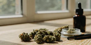Fleurs de cannabis riches en résine accompagnées d’un flacon compte-gouttes et d’un récipient en verre sur une table en bois