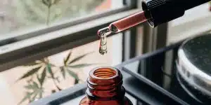 Huile de cannabis versée avec une pipette dans un flacon en verre ambré, sur une surface intérieure éclairée naturellement.