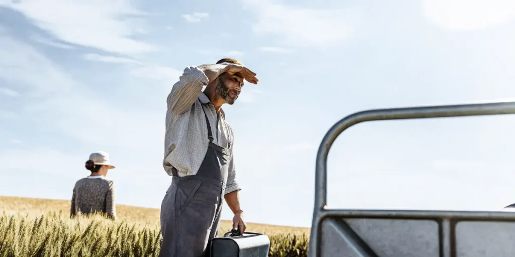 Agriculteur champ ble soleil tenant valise et protegeant yeux sous ciel clair.